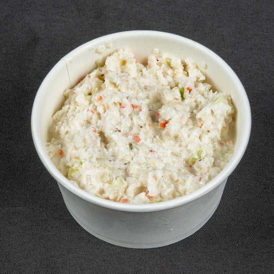 Creamy coleslaw with shredded cabbage, carrots, and green vegetables served in a white bowl on a dark surface.