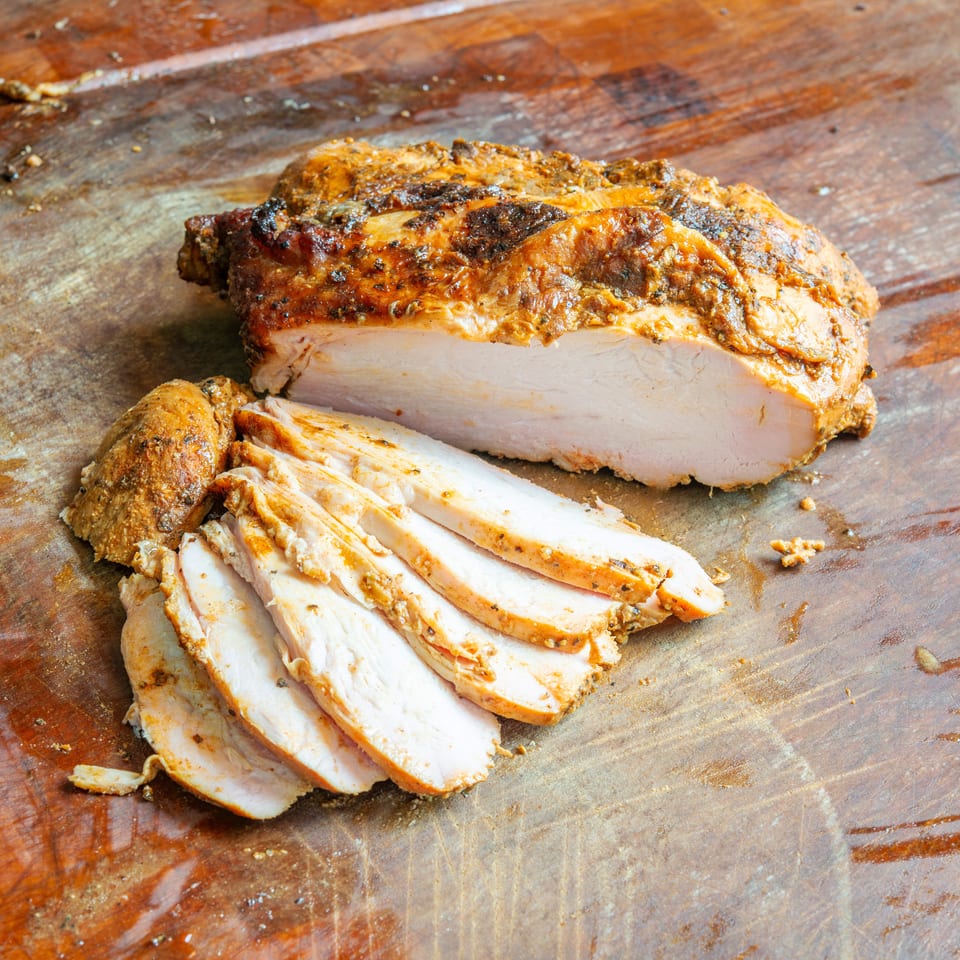 Sliced roasted chicken breast with a seasoned, browned crust arranged on a rustic wooden cutting board.