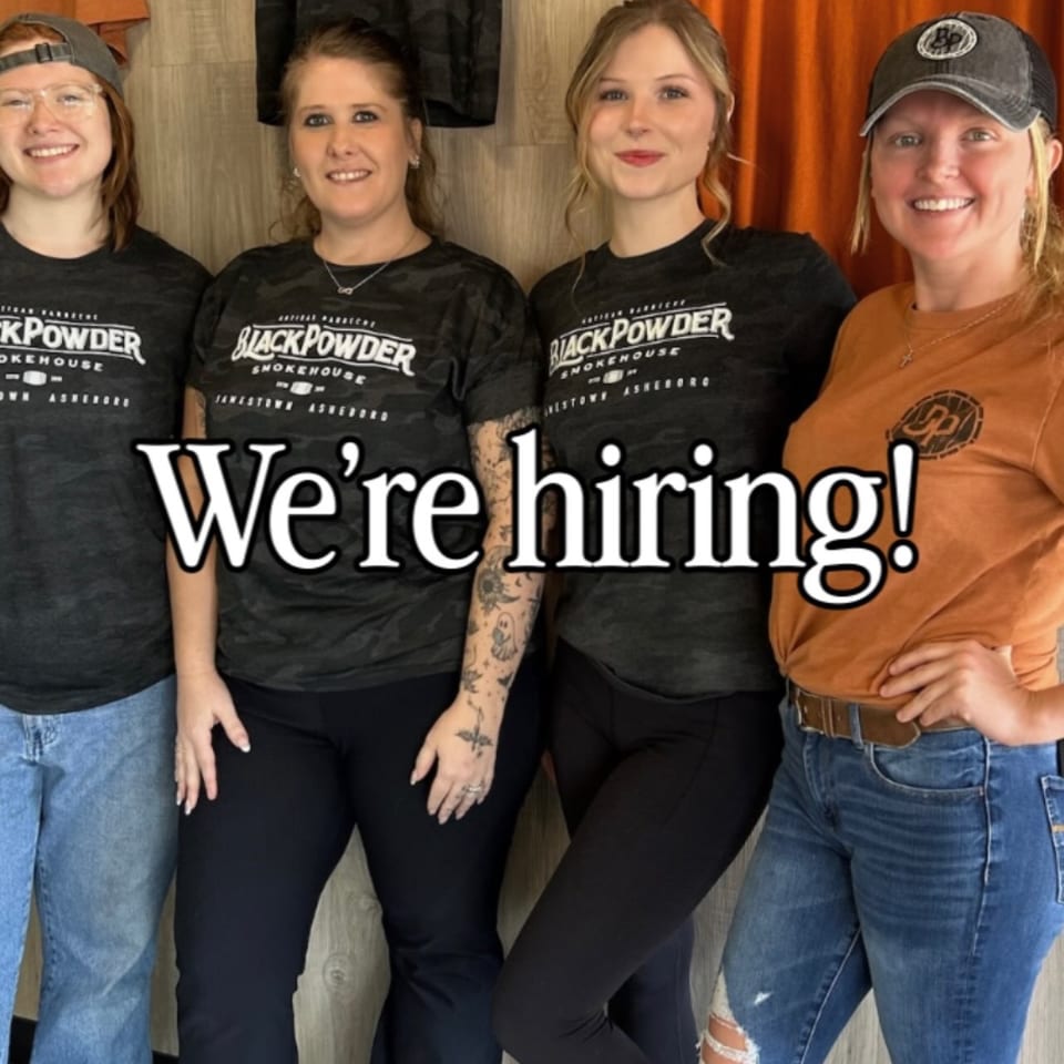 Four smiling Black Powder Smokehouse employees stand together, with "We're hiring!" overlaid.