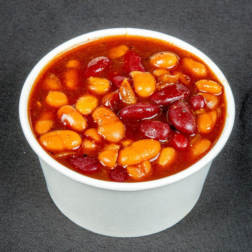 Close-up of red kidney beans and golden beans simmered in a rich reddish sauce inside a white bowl.