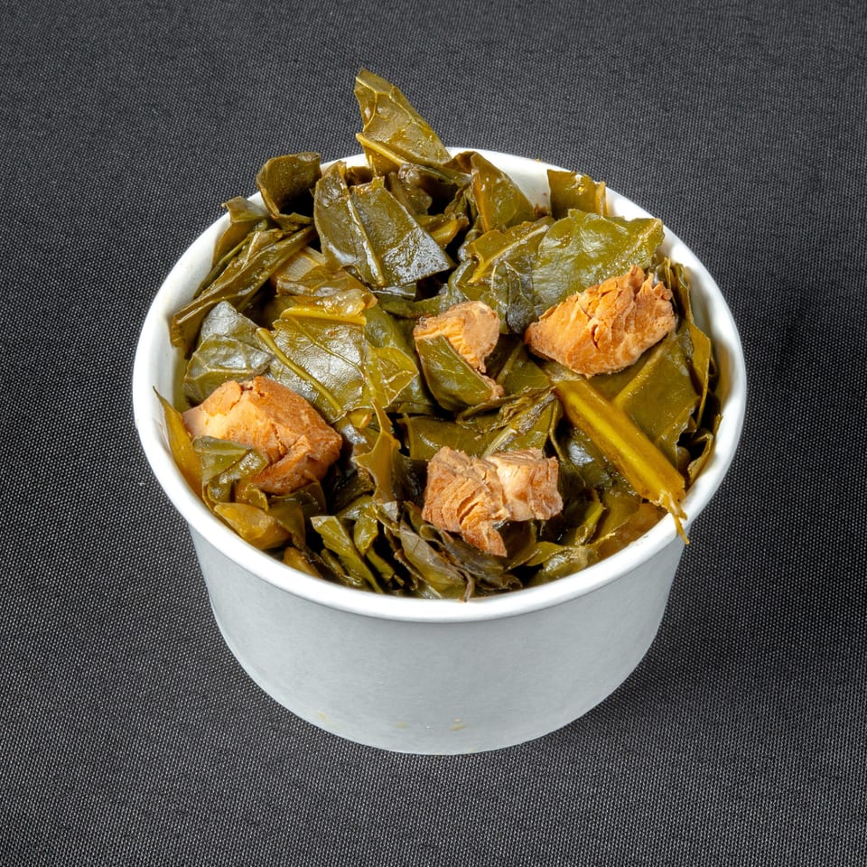 Bowl of cooked leafy greens topped with chunks of tender meat on a dark textured surface.
