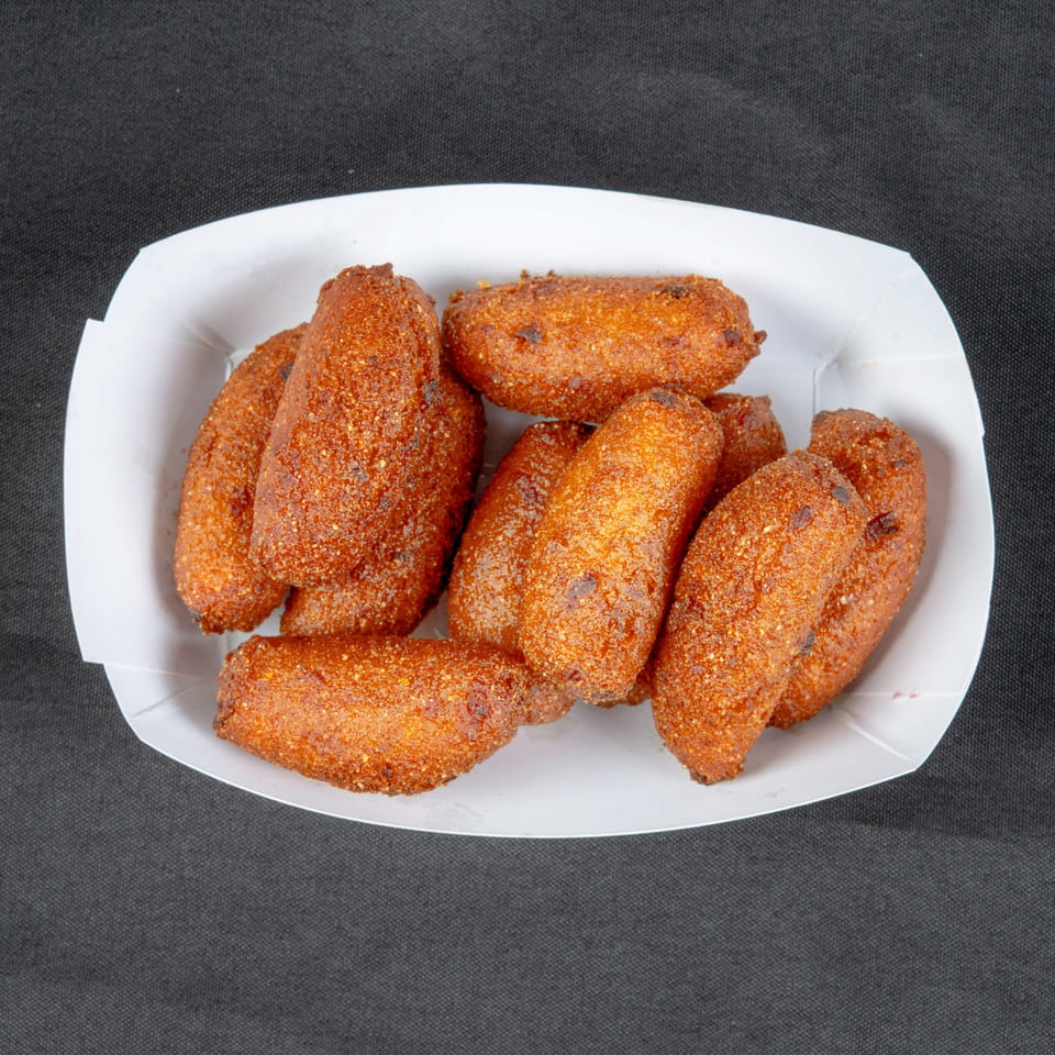 A pile of golden-brown, seasoned fried snacks sits in a white paper tray on a dark surface.