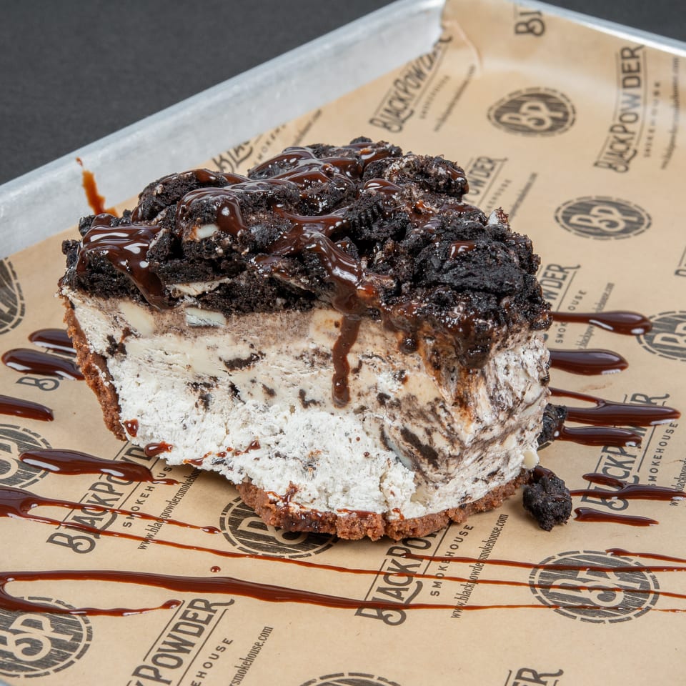 Chocolate cookie ice cream cake topped with cookie crumbles and chocolate drizzle on Black Rock Smokehouse paper.