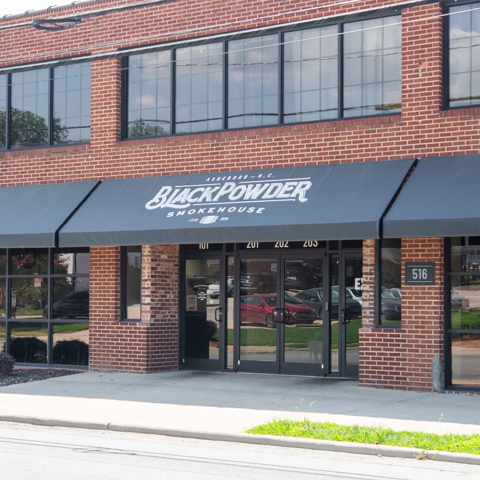 Brick storefront of Black Powder Smokehouse in Asheboro, North Carolina, featuring black awnings, glass doors, and address 516.